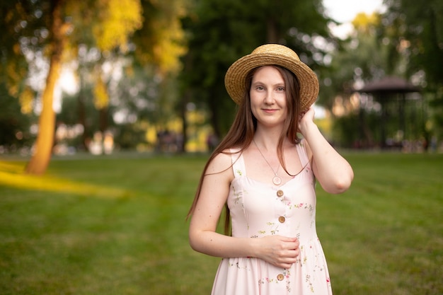 Schönes Mädchen in Kleid und Hut vor dem Hintergrund eines sonnenbeschienenen Gartens