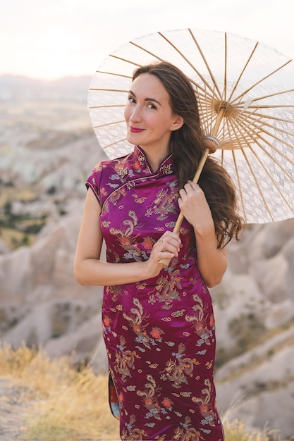 Schönes Mädchen in nationaler chinesischer Kleidung vor dem Hintergrund der Berge mit einem Regenschirm in der Hand