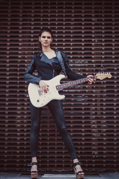 Schönes Mädchen in schwarzer Kleidung posiert mit E-Gitarre