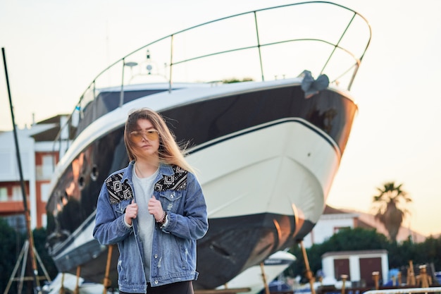 Schönes Mädchen in Sonnenbrille und Jeansjacke mit langen blonden Haaren in einem Sommersonnenuntergang