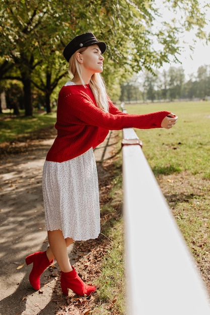 Schönes Mädchen in stilvollen roten Schuhen und trendigem Kleid, das zärtlich posiert Schöne blonde Frau, die sich im Park entspannt