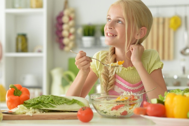 Schönes Mädchen isst Salat in der Küche