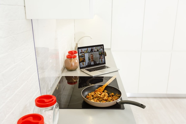 Schönes Mädchen lernt, gesundes Essen online über das Internet von einem Laptop in der grauen Küche auf dem Tisch zu kochen.