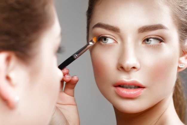 Schönes Mädchen macht sich ein Make-up im Spiegel Schönheitsgesicht Foto im Studio aufgenommen