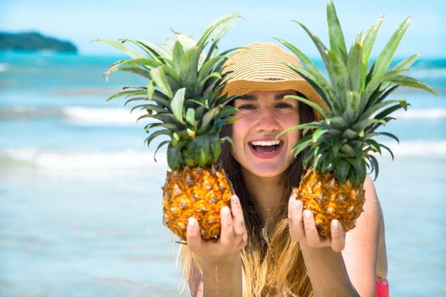 Schönes mädchen mit ananas an einem exotischen strand, eine fröhliche stimmung und ein schönes lächeln