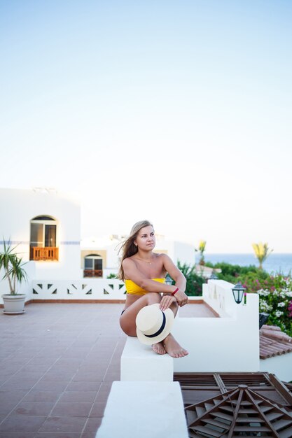 Schönes Mädchen mit blonden Haaren und in einem gelben Badeanzug entspannt sich auf einer Terrasse gegen das Meer