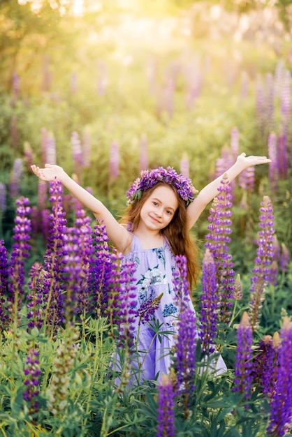 Schönes Mädchen mit Blumen in ihrem Haar unter den Blumen. Sonniges Sommerfoto mit einem Kind in den lila Blumen