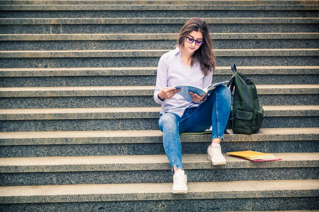 Schönes Mädchen mit Brille, mit Büchern, sitzt auf der Treppe