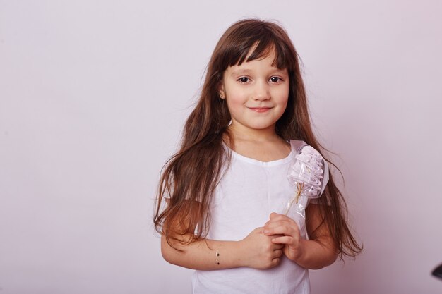 Schönes Mädchen mit dem blonden Haar isst einen Lutscher, rundes Karamell auf Stock in den Händen des netten lächelnden Mädchens. Baby mit dem langen Haar im weißen T-Shirt leckt Lutscher. Russland, Swerdlowsk, 1. Dezember 2018