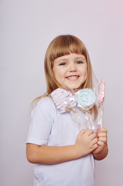 Schönes Mädchen mit dem blonden Haar isst einen Lutscher, rundes Karamell auf Stock in den Händen des netten lächelnden Mädchens