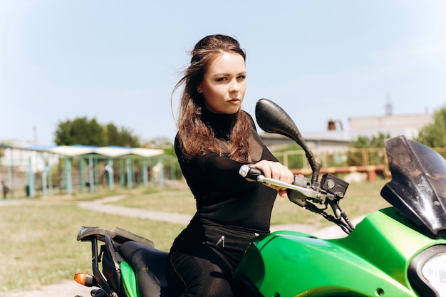 Schönes Mädchen mit dunklen Haaren sitzt auf einem grünen Motorrad..