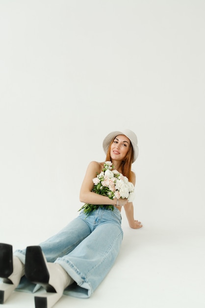 Schönes Mädchen mit einem Blumenstrauß in einem Hut und einer blauen Jeans