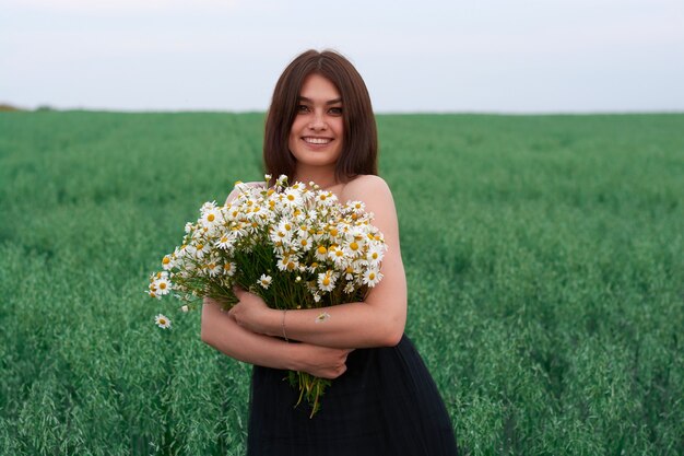 Schönes Mädchen mit einem Blumenstrauß von Gänseblümchen in einem Blumenfeld.