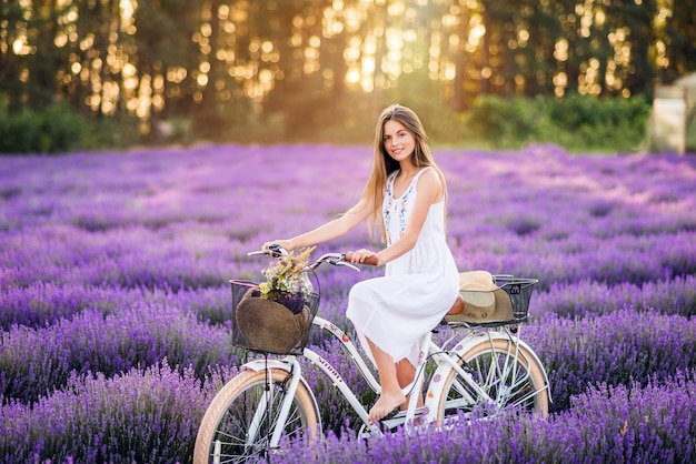 Schönes Mädchen mit einem Fahrrad in einem Lavendelfeld. Nettes Mädchen auf lila Hintergrund.