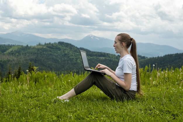 Schönes Mädchen mit einem Laptop, der auf grünem Gras sitzt