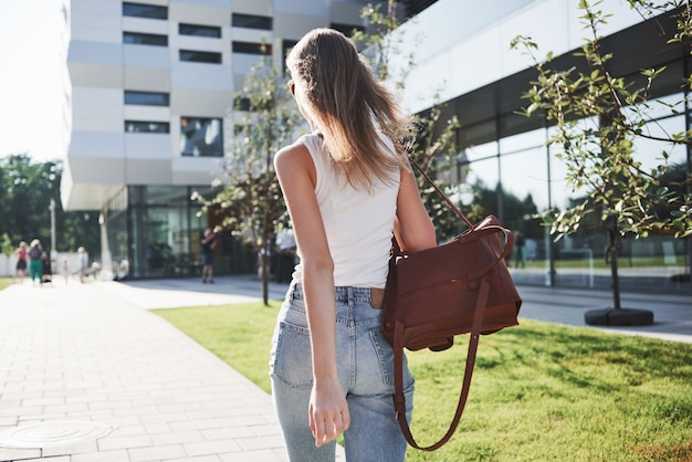 Schönes Mädchen mit einem Rucksack, das entlang der Stadtstraße an einem sonnigen Morgen geht.