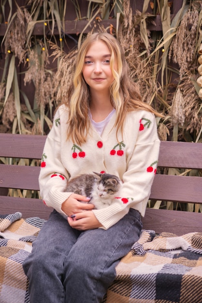 schönes Mädchen mit einer Katze draußen im Herbst nahe dem Haus auf der Bank