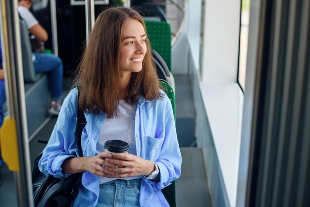 Schönes Mädchen mit einer Tasse köstlichem Kaffee fährt mit öffentlichen Verkehrsmitteln zur Universität