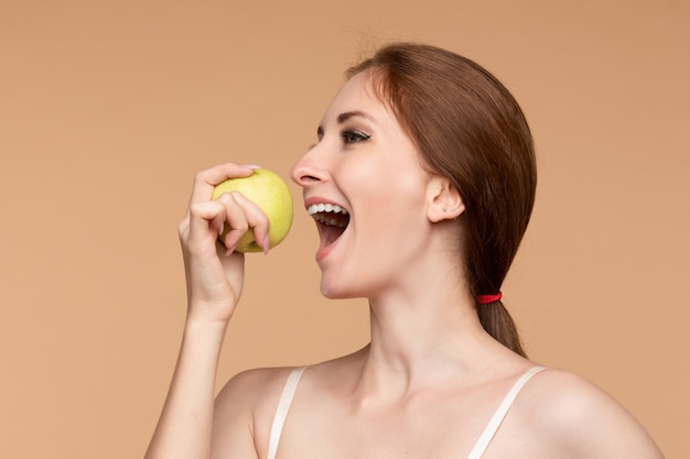 Schönes Mädchen mit gebundenem Rückenhaar, das leckeren Apfel isst.