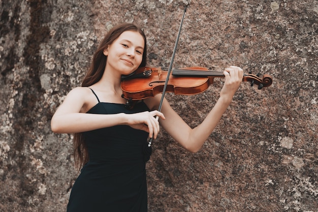 Schönes Mädchen mit Geige, das in der Natur lächelt. Foto in hoher Qualität