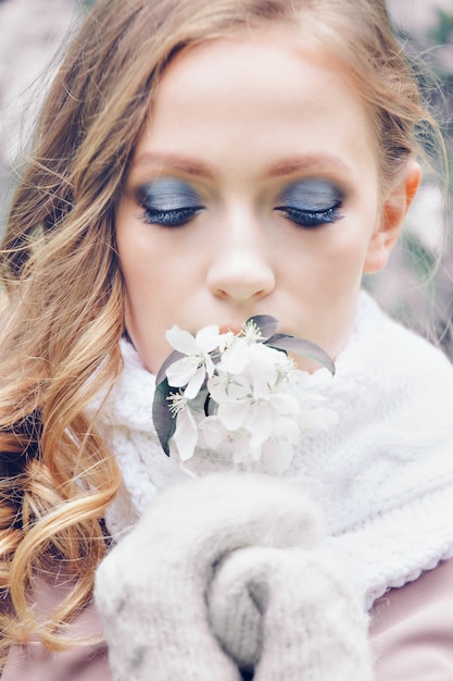 Schönes Mädchen mit hellem Make-up in einem warmen Schal und in Handschuhen, die Blumen halten