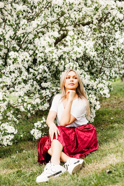 Foto schönes mädchen mit hellen haaren, brille, in der nähe von blühenden bäumen, apfelbaum, frühling, ästen, blumen, mode, stil, europäisch, rot