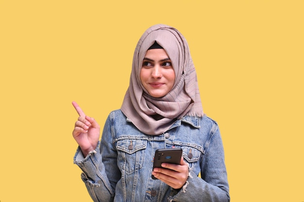 Schönes Mädchen mit Hijab mit Jeansjacke, das ein indisches pakistanisches Telefonmodell hält