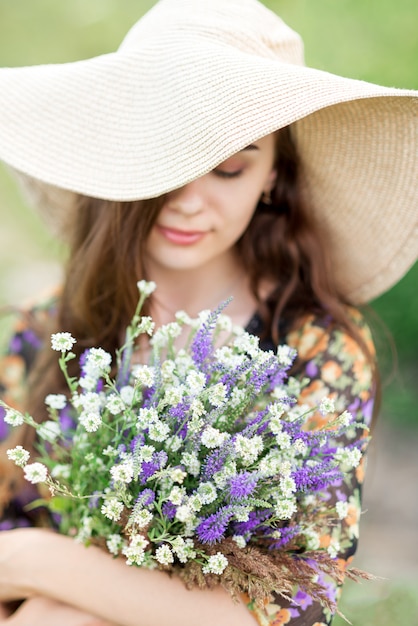 Schönes Mädchen mit Hut mit einem Blumenstrauß von weißen und lila Blumen