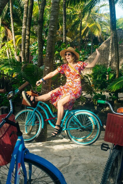 Schönes Mädchen mit Hut und hellem Kleid auf einem Fahrrad im Dschungel