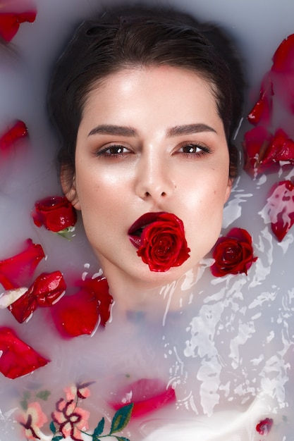 Schönes Mädchen mit klassischem Make-up und roten Lippen im Badezimmer mit Blumen. Schönheitsgesicht. Foto im Studio aufgenommen