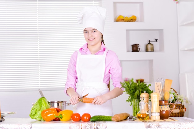 Schönes Mädchen mit Kochuniform, das in der Küche kocht