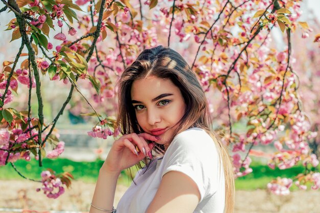 Schönes Mädchen mit langen Haaren genießt die Schönheit der Frühlingsnatur nahe dem blühenden Sakura-Baum.