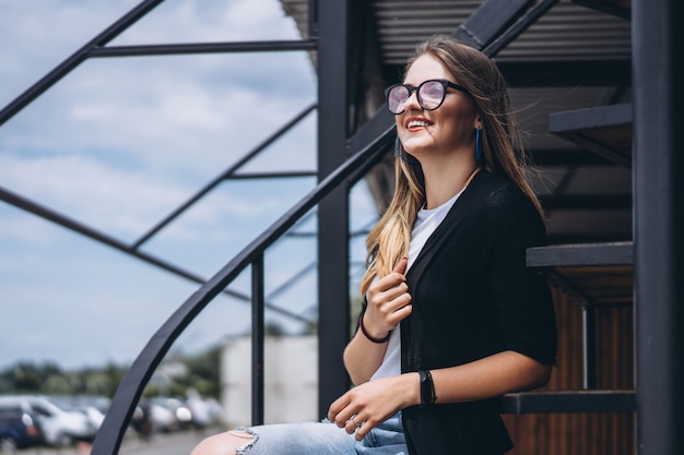 Schönes Mädchen mit langen Haaren und Brille, die auf Metalltreppen sitzen