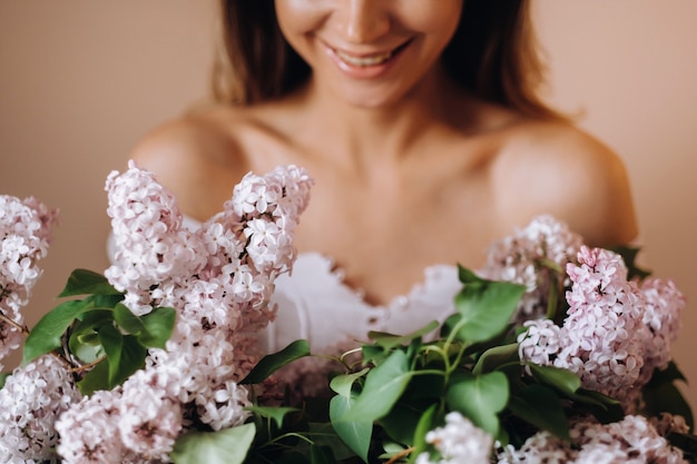 Schönes Mädchen mit lila Blumen in ihren Händen. Ein Mädchen mit lila Blumen im Frühjahr zu Hause. Ein Mädchen mit langen Haaren und Flieder in den Händen.