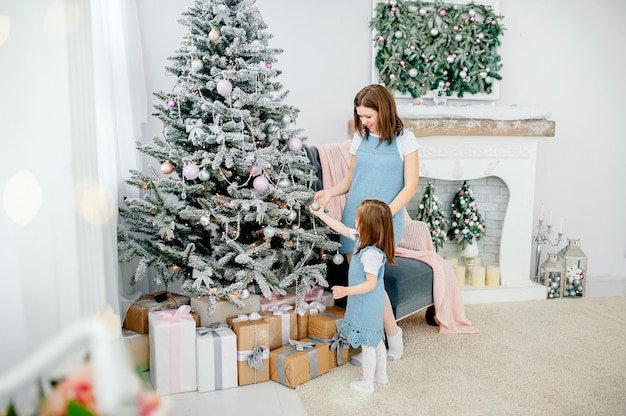 Schönes Mädchen mit Mutter schmückt den Weihnachtsbaum zu Hause. Glückliche Familie. Frohe Weihnachten und ein glückliches Neues Jahr.