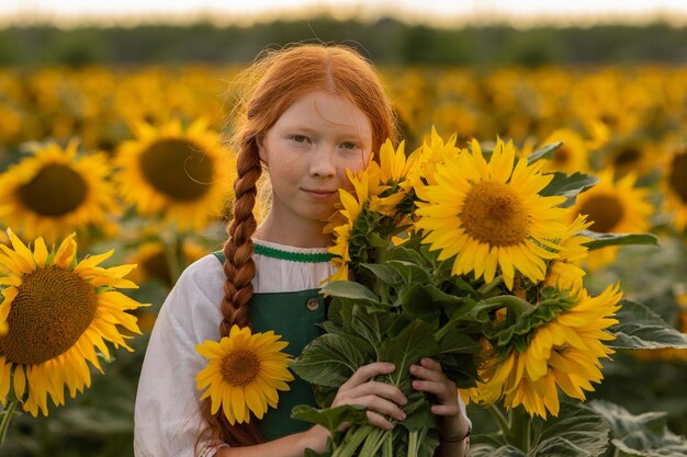 Schönes Mädchen mit roten Haaren und Sommersprossen steht auf einem Feld mit Sonnenblumen