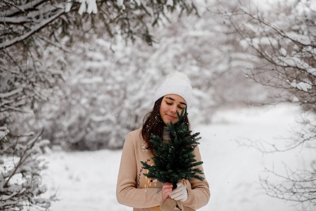 Schönes Mädchen mit Schlittenweihnachtsbaum und Geschenken im Winter in einem verschneiten Wald