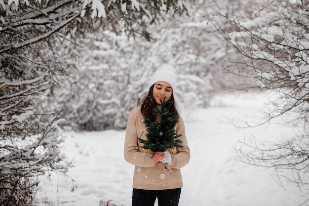 Schönes Mädchen mit Schlittenweihnachtsbaum und Geschenken im Winter in einem verschneiten Wald