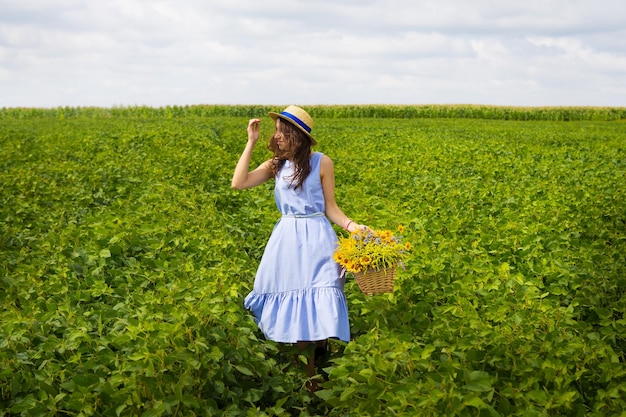 Schönes Mädchen mit Strohhut steht auf einem grünen Feld mit einem Blumenstrauß