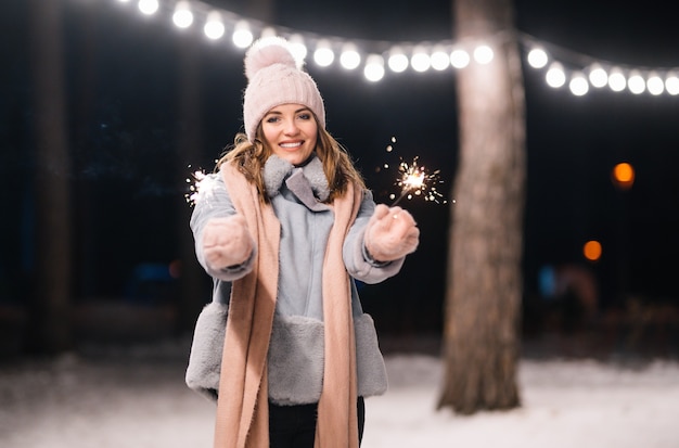 Schönes Mädchen mit Wunderkerzen in den Händen Fröhliche Winterzeit im Wald Festliche Girlandenlichter