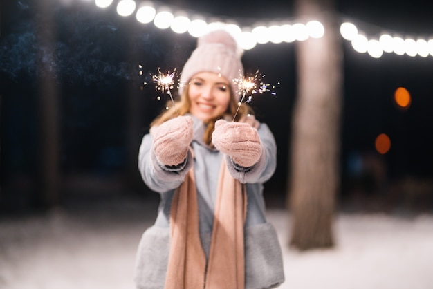 Schönes Mädchen mit Wunderkerzen in den Händen Fröhliche Winterzeit im Wald Festliche Girlandenlichter