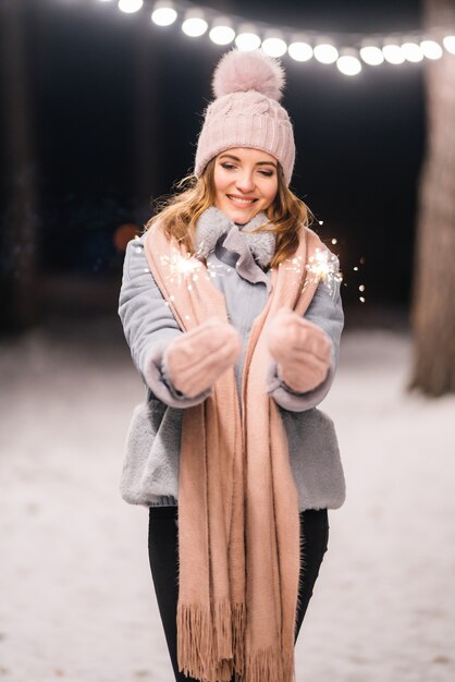 Schönes Mädchen mit Wunderkerzen in den Händen Fröhliche Winterzeit im Wald Festliche Girlandenlichter