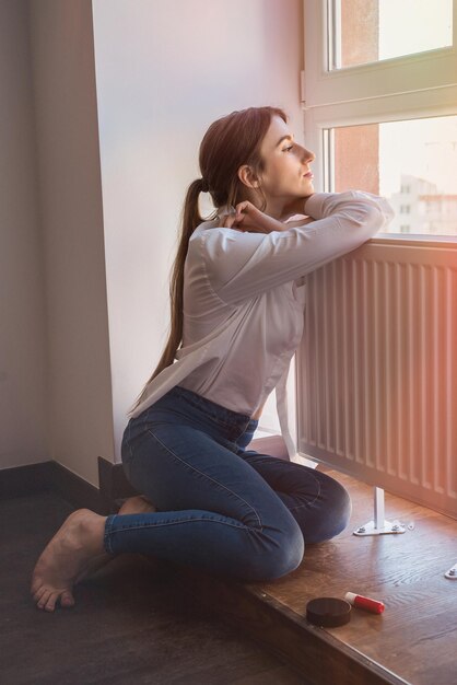 Schönes Mädchen posiert am Fenster und genießt die Sonne