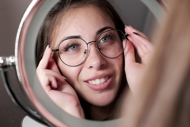 Schönes Mädchen probiert eine Brille an, während sie sich im Spiegel bewundert Brillengeschäft Augenklinik