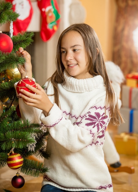 Schönes Mädchen schmückt Weihnachtsbaum im Wohnzimmer