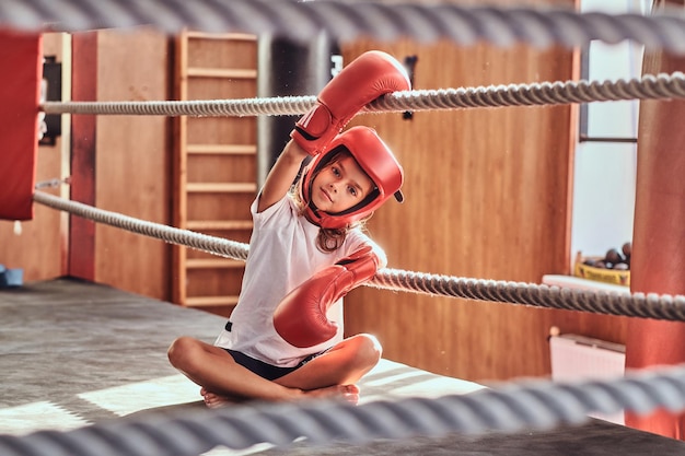 Schönes mädchen sitzt auf boxring und trägt boxeruniform - handschuhe und helm.