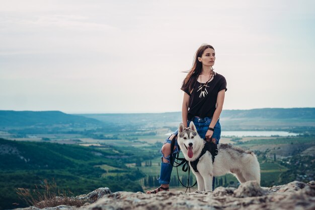 Schönes Mädchen spielt mit einem Hund grau und weiß Husky in den Bergen bei Sonnenuntergang