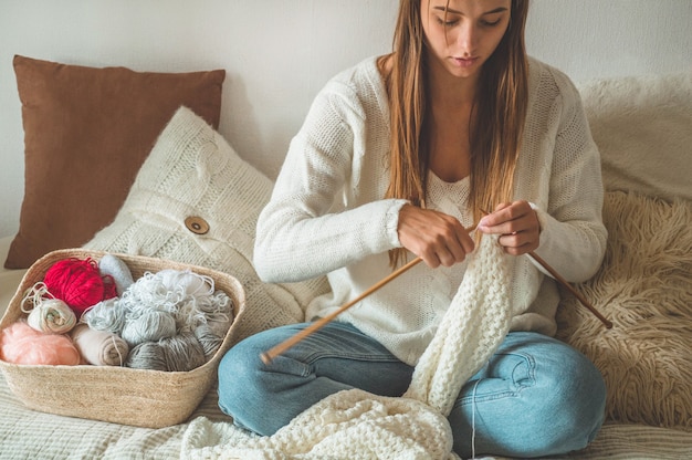 Foto schönes mädchen strickt einen warmen pullover auf dem bett. stricken als hobby. zubehör zum stricken.