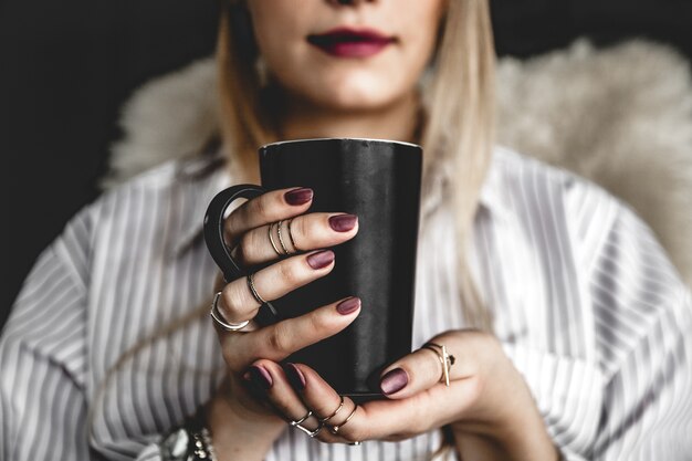 Schönes Mädchen trinkt Kaffee mit einer schwarzen Tasse im Hemd, Mode, Essen