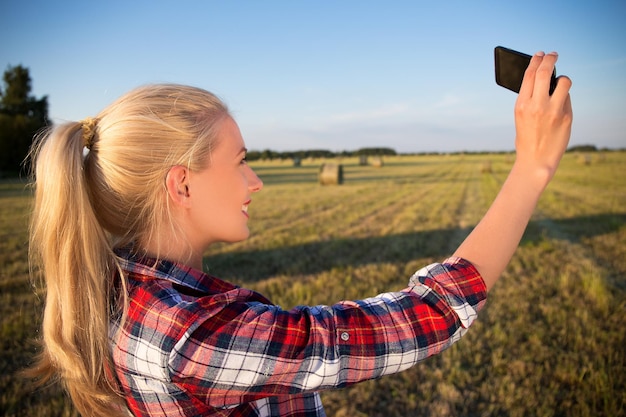 Schönes Mädchen vom Land macht Selfie-Foto auf dem Smartphone im Feld mit Heuhaufen